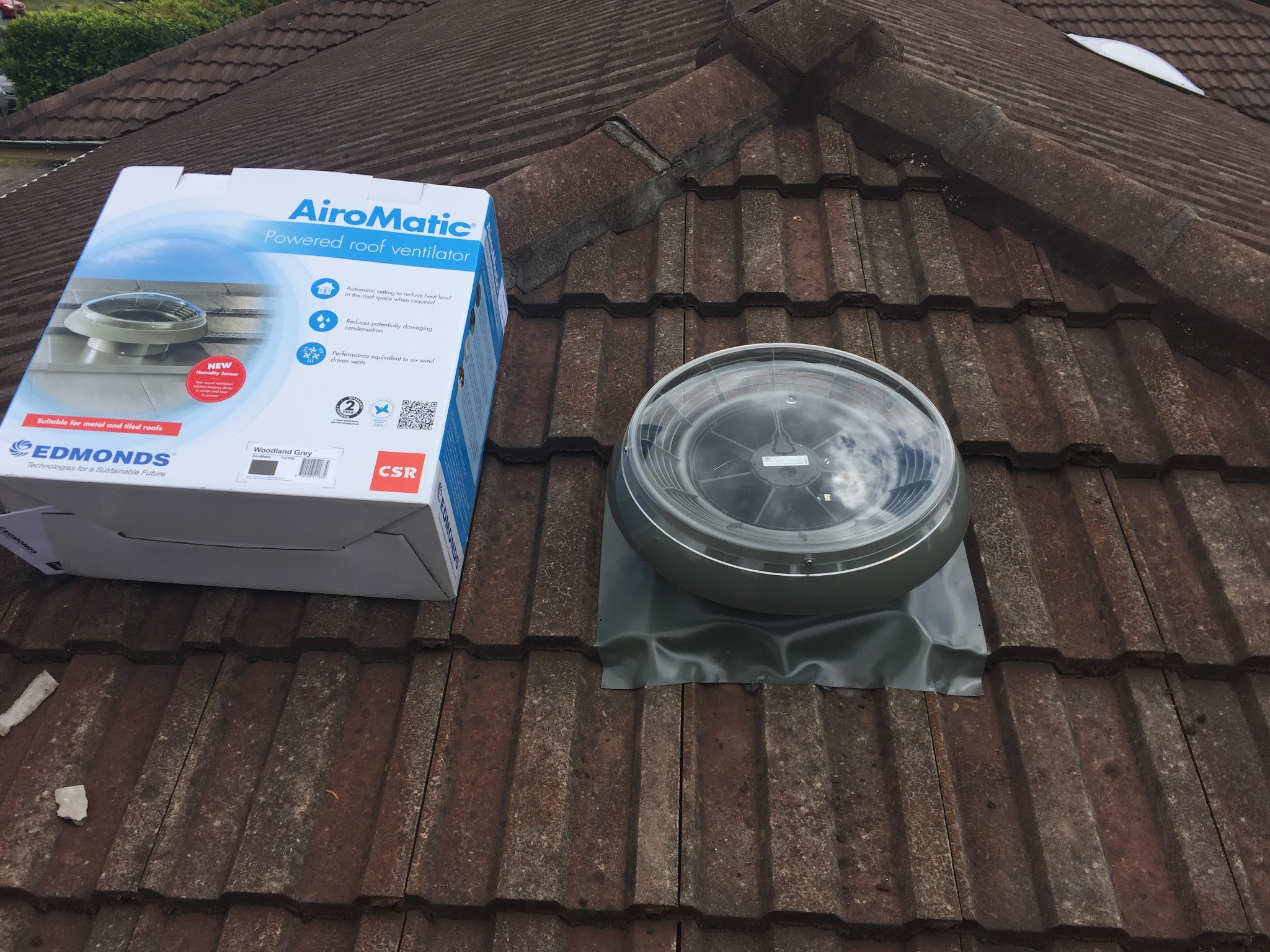 Powered roof ventilator fitted into a tiled roof beside its box
