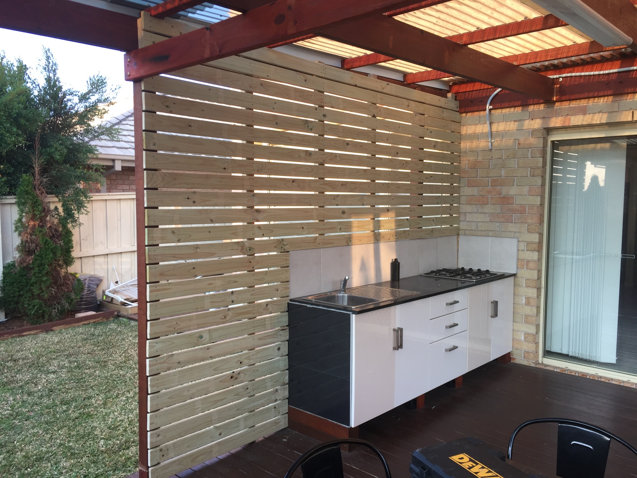 Outdoor kitchen with sink, gas cooktop and cabinets under a timber pergola