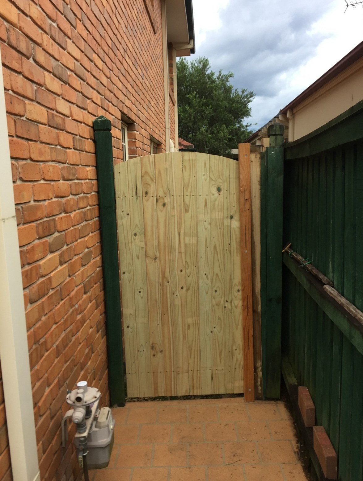 New timber side gate fitted between a brick house and a green timber fence