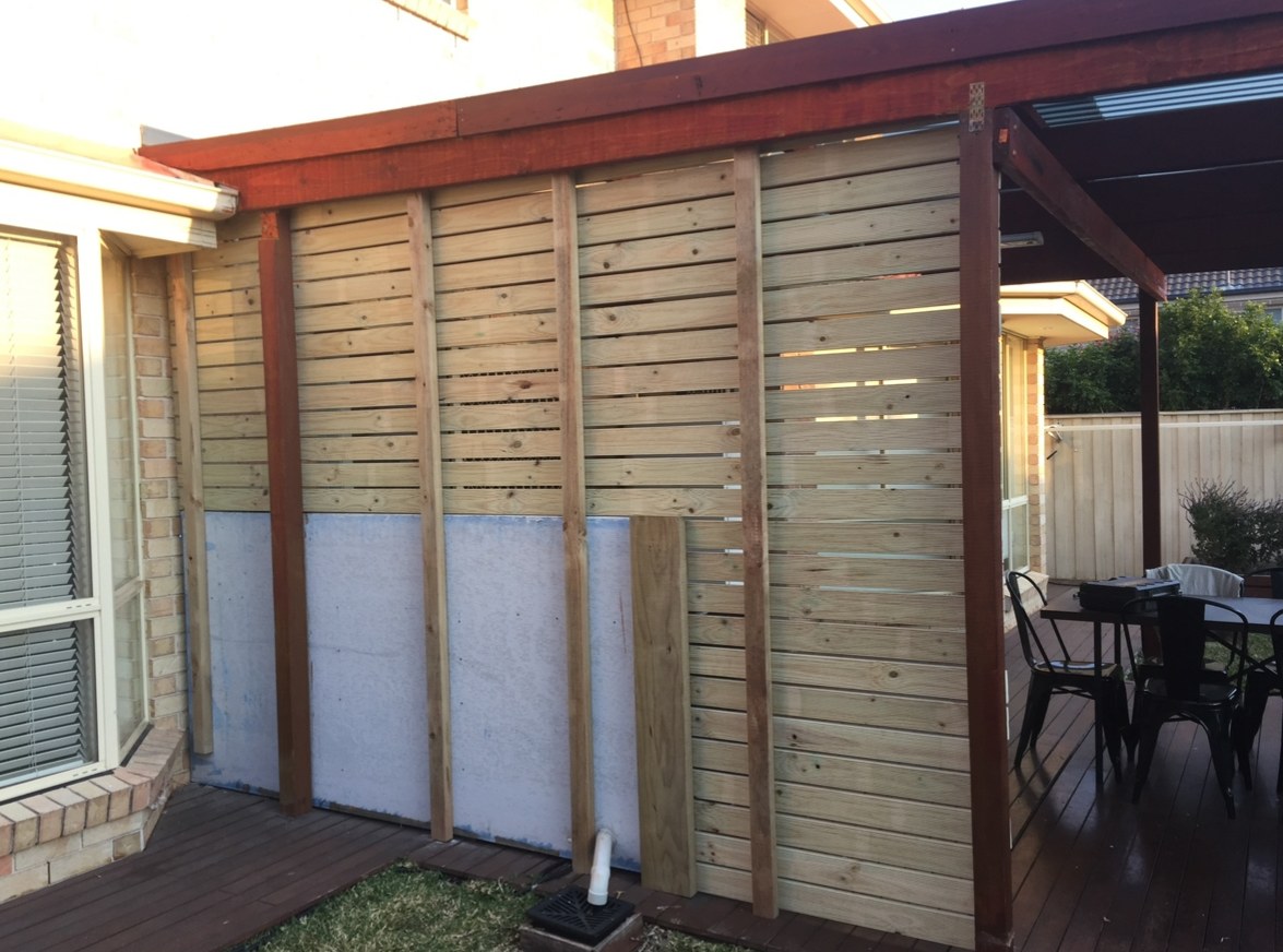 Slatted timber privacy screen being built onto a pergola beside a brick house