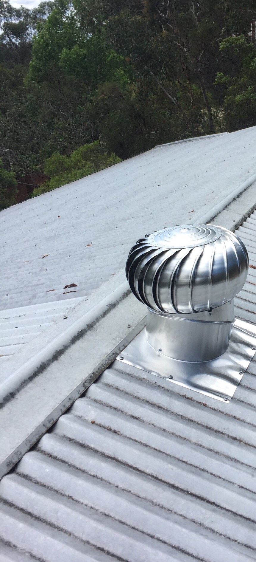 Newly installed whirlybird on a corrugated metal roof with trees behind